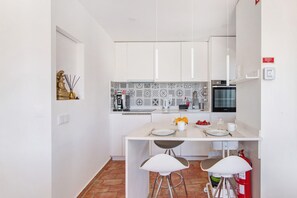 Une cuisine moderne avec des meubles blancs, un pare-feu décoré, un four à micro-ondes et un petit coin repas équipé de tabourets.