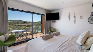 Un dormitorio con una cama grande, un televisor montado en la pared y un balcón con una mesa y sillas.
