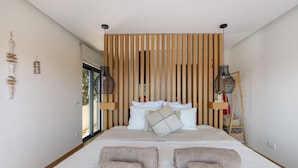 Un dormitorio con cama, almohadas, un cabecero de listones de madera y dos lámparas colgantes.