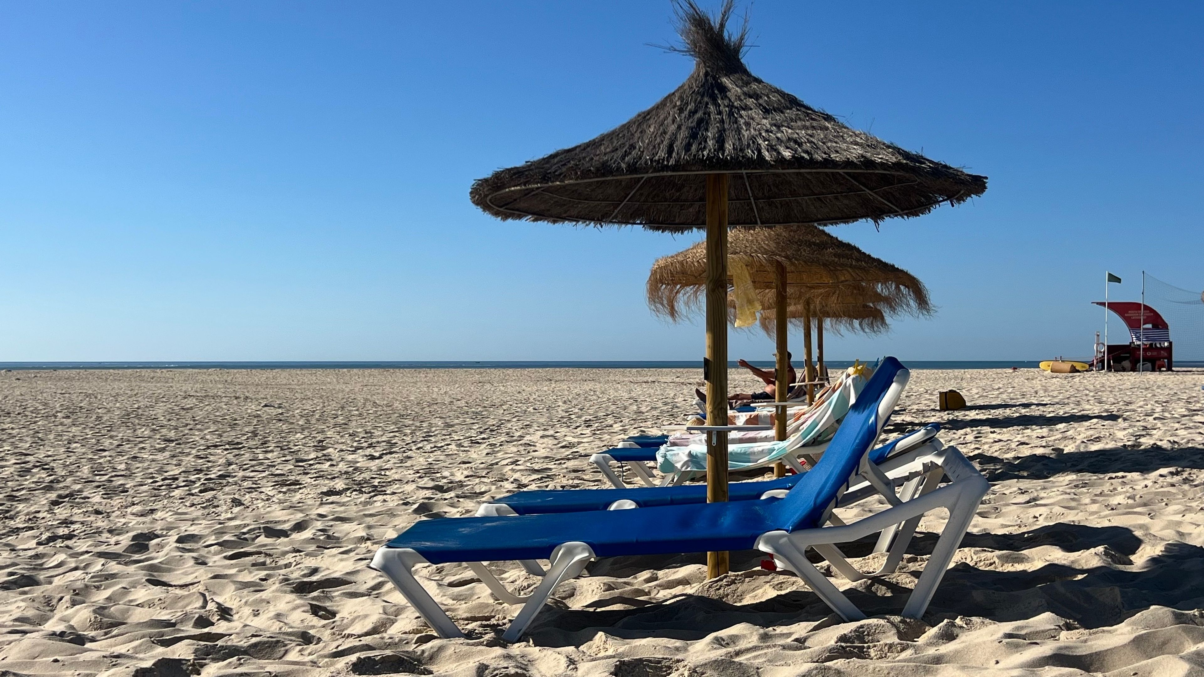 A beach with thatched umbrellas, lounge chairs, and a lifeguard station.