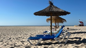 Ein Strand mit Reetsonnenstühlen, Liegen und einem Rettungsschwimmerstand.