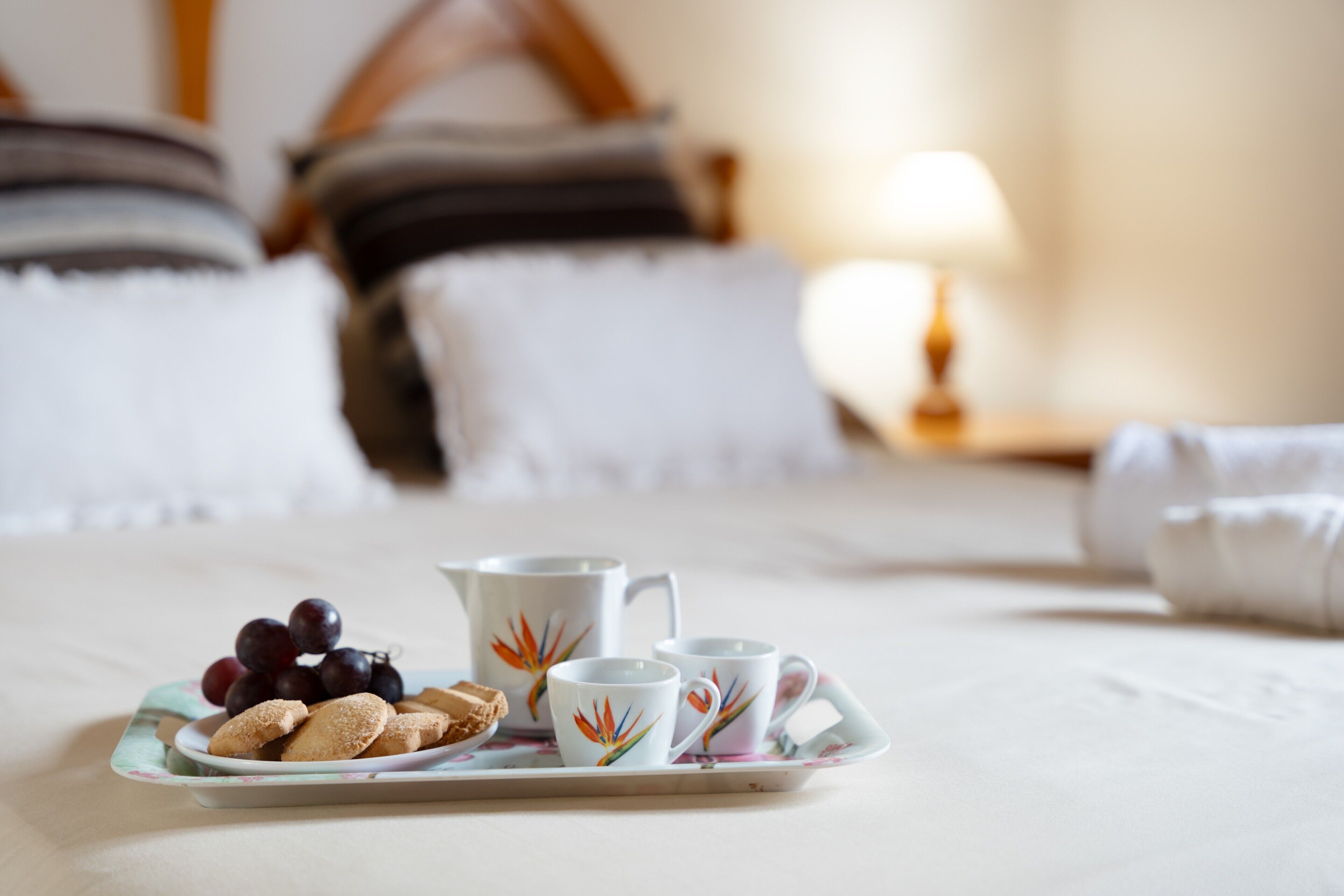 Un plateau avec des biscuits et des raisins, posé sur un lit agrémenté d’oreillers et éclairé par une lampe, dans une chambre d’hôtel.
