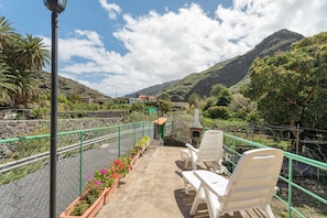 Eine Terrasse mit weißen Stühlen und einem Grill, mit Blick auf eine gebirgige Landschaft.