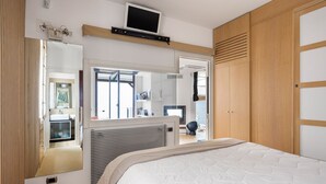 A bedroom with a bed, a TV mounted on the wall, a wardrobe, and a mirror.