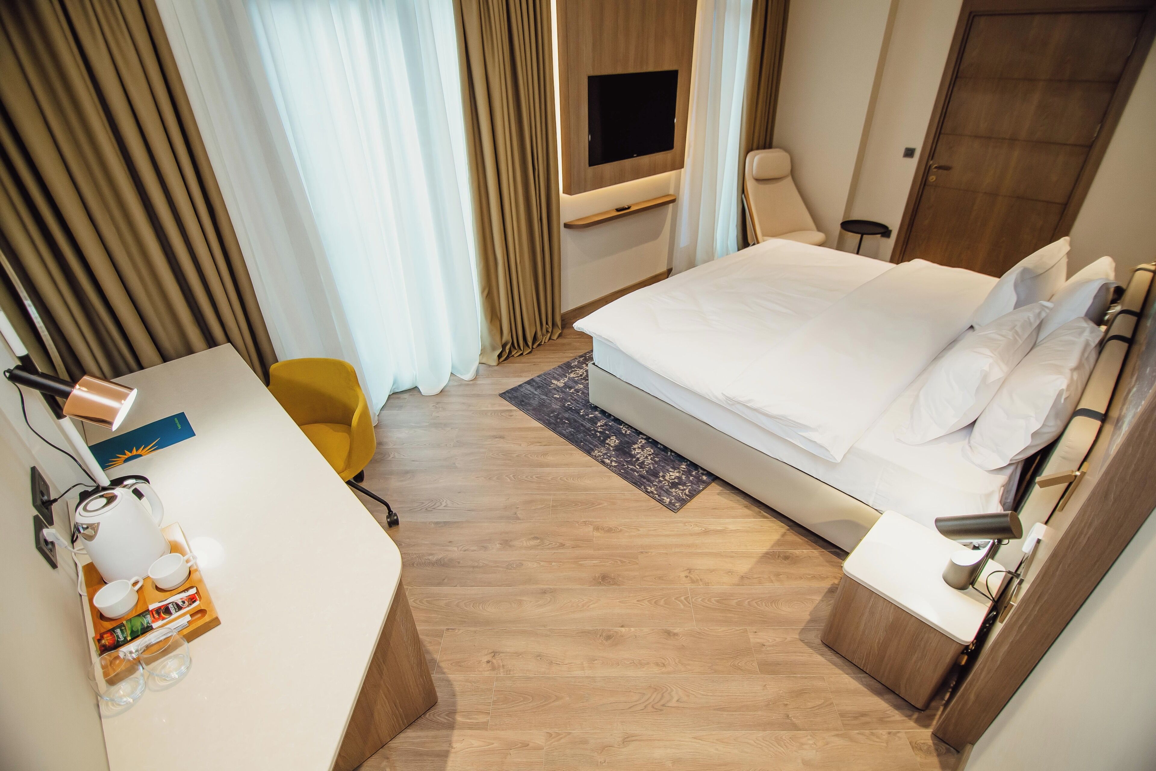 Ein Hotelzimmer mit einem Bett, einem Schreibtisch mit Kaffeemaschine, einem Fernseher und einem Sessel.