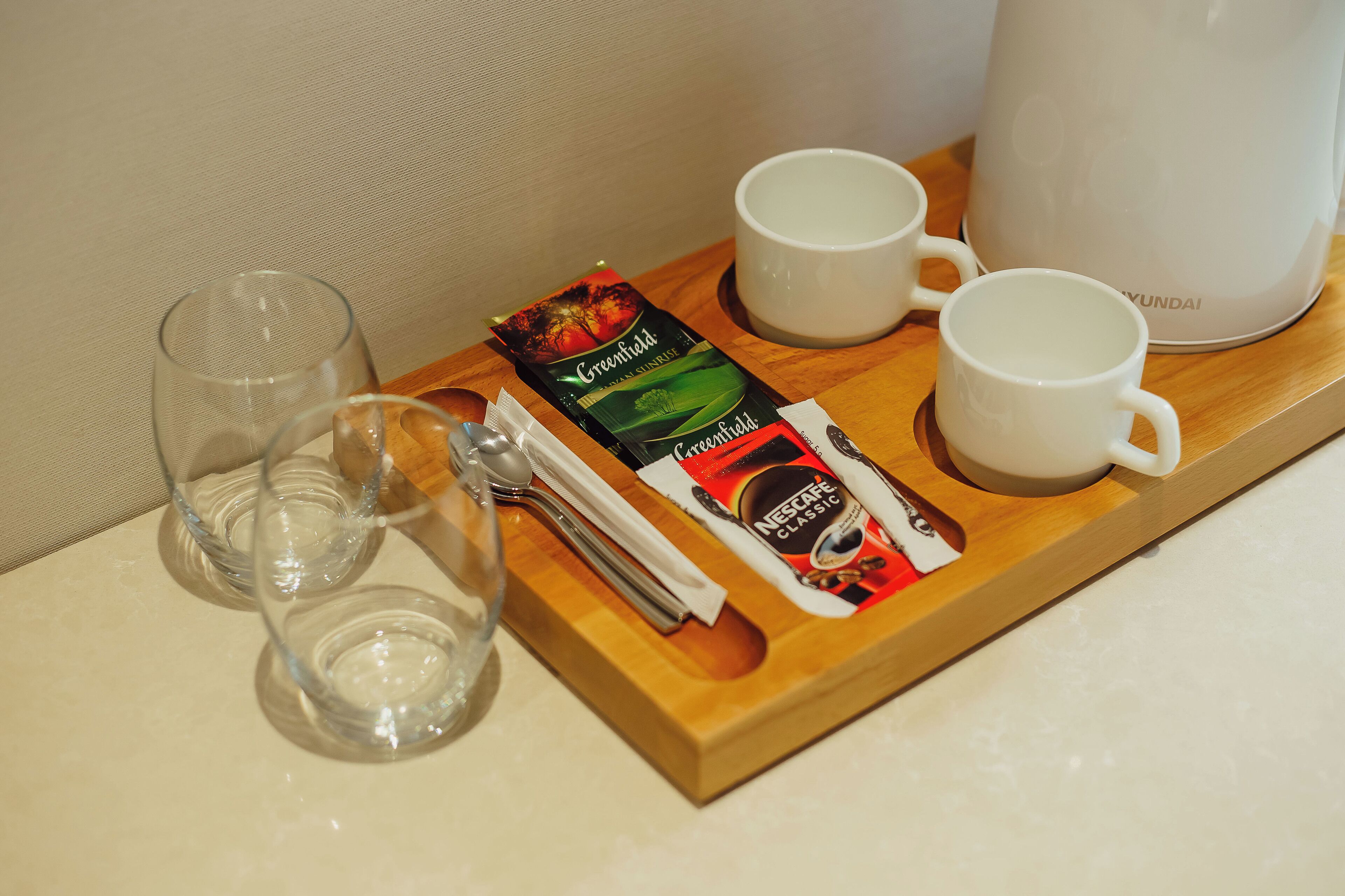 A tray with two white mugs, a Nescafé Classic coffee sachet, and a greenfield coffee sachet.