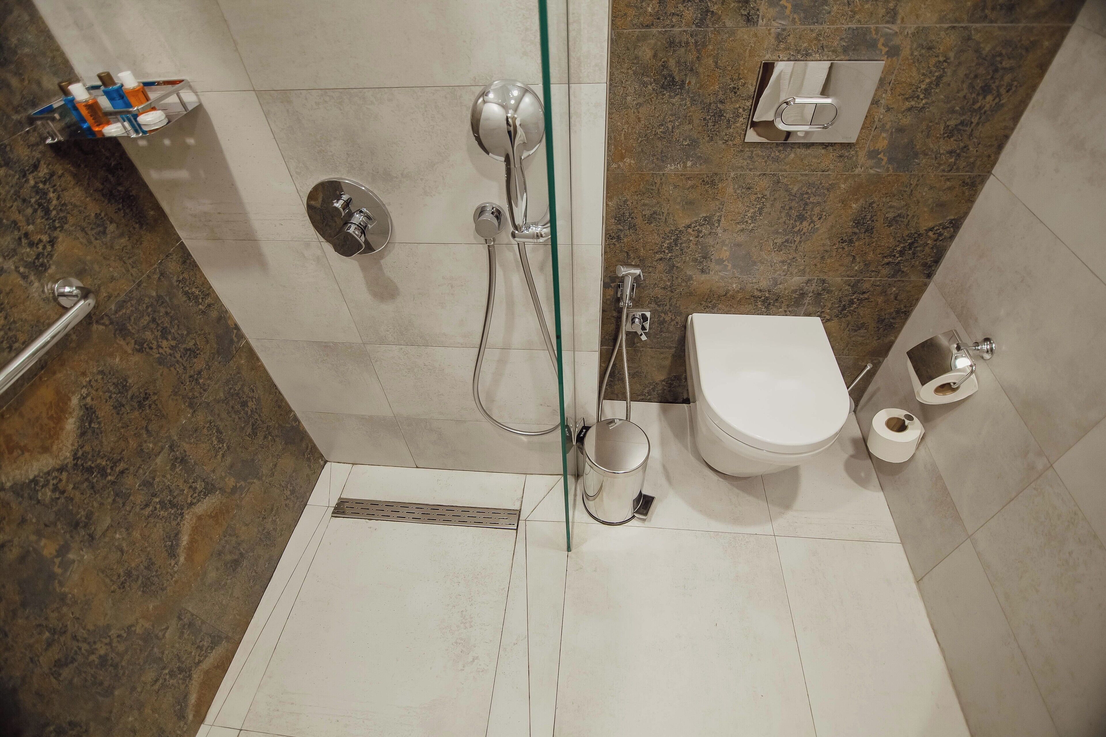 Et badeværelse med bruser, toilet og glasvæg.
