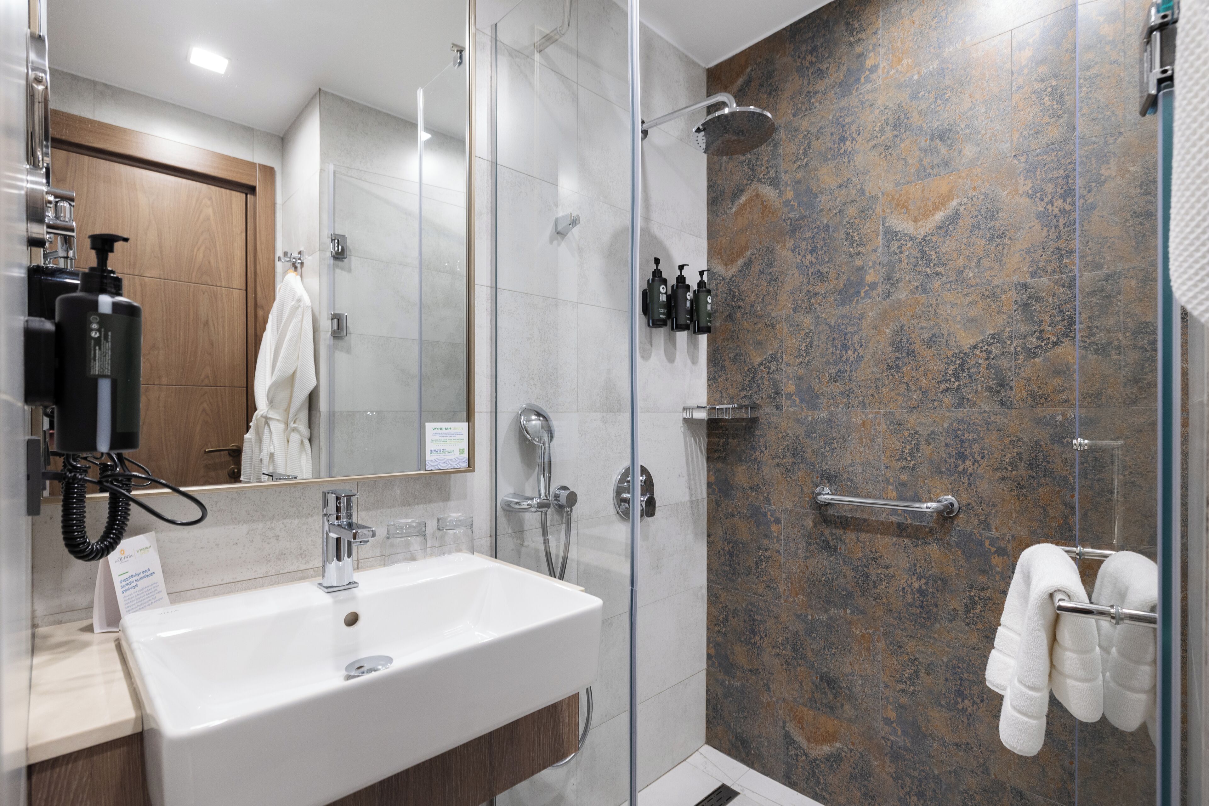 A modern bathroom with a glass shower enclosure, a white sink, and a mirror.
