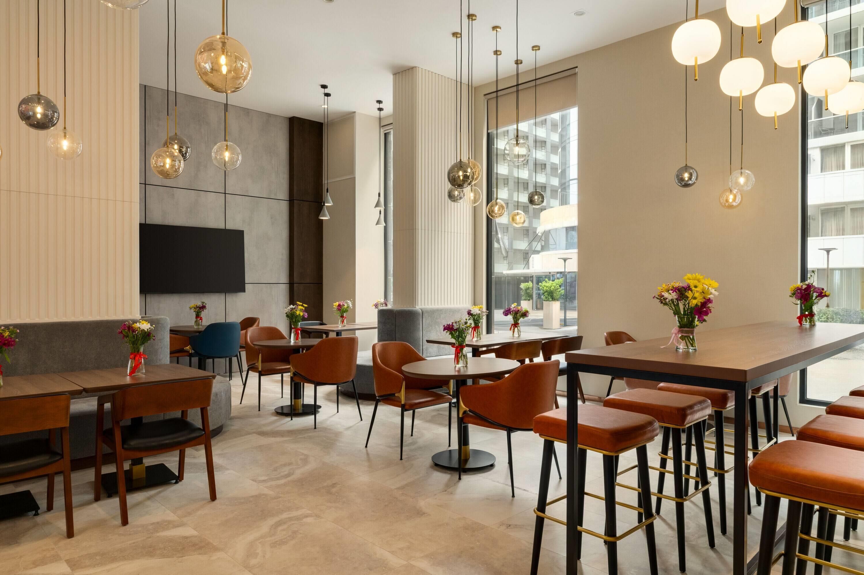 A modern restaurant with high tables and bar stools, large windows, and hanging spherical light fixtures.