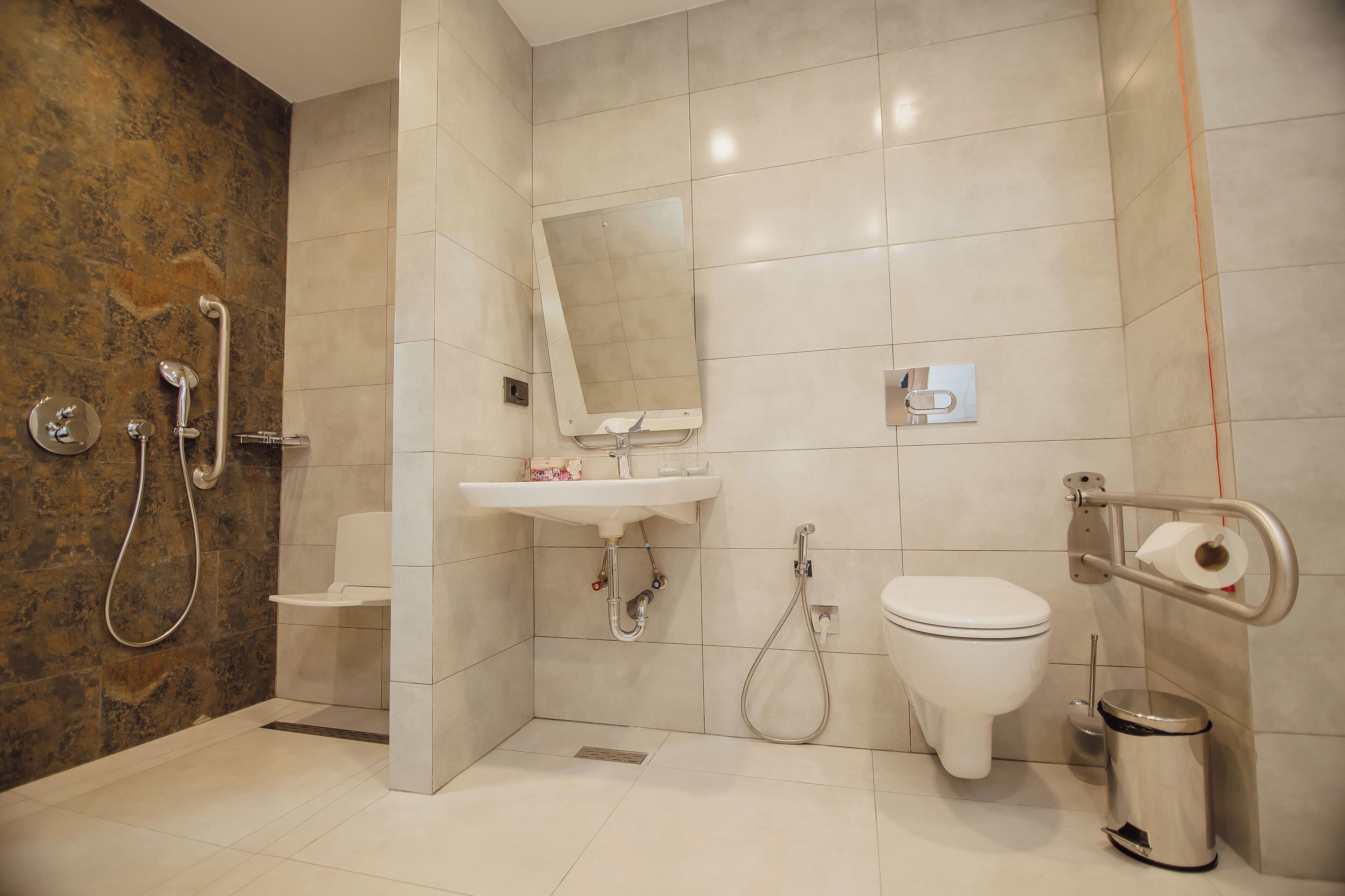 Ein modernes Badezimmer mit Dusche, Toilette, Waschbecken und einer Haltestange zur Barrierefreiheit.