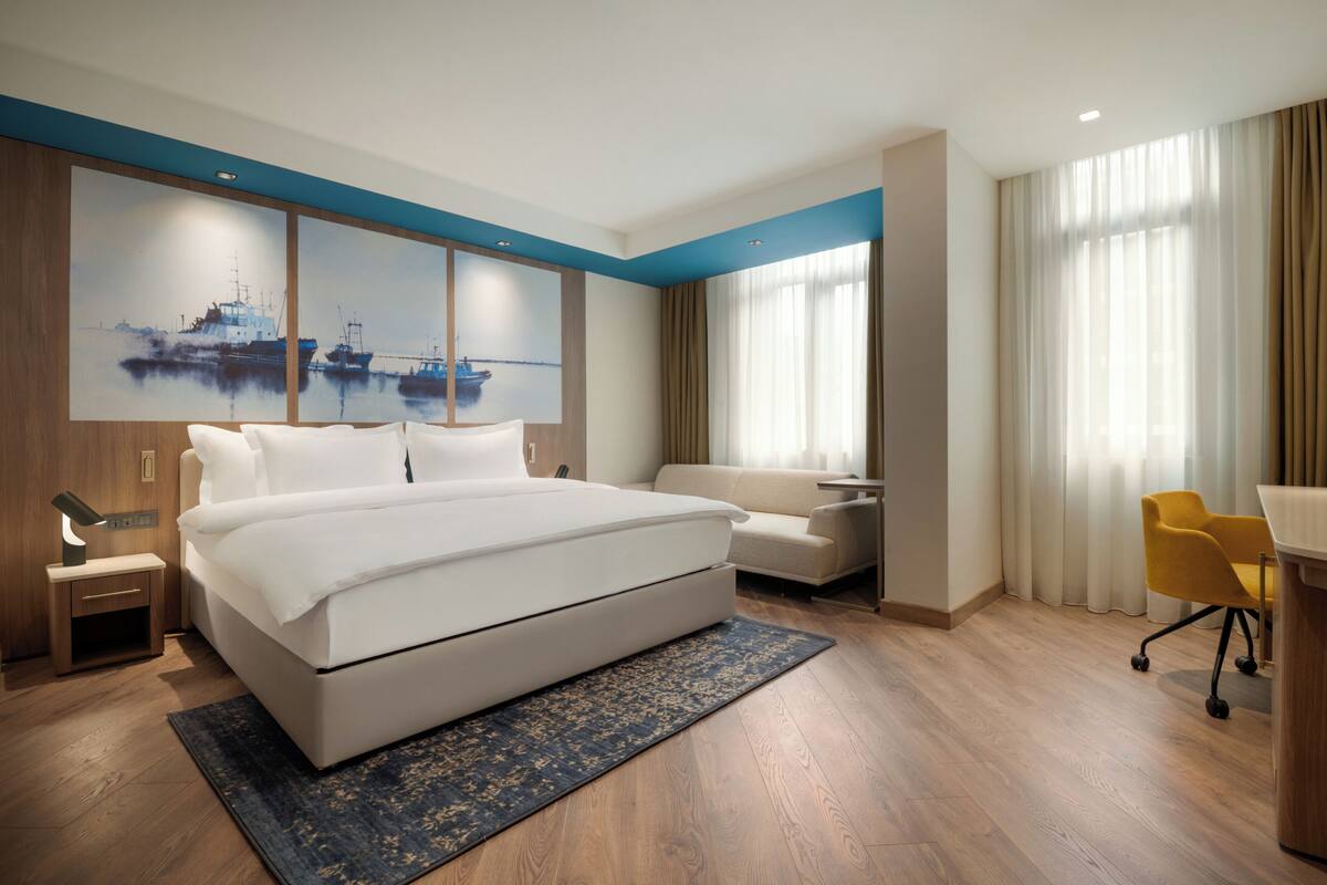 Una camera d'albergo moderna con un letto grande, una scrivania, una sedia e un quadro con dei battelli sulla parete.