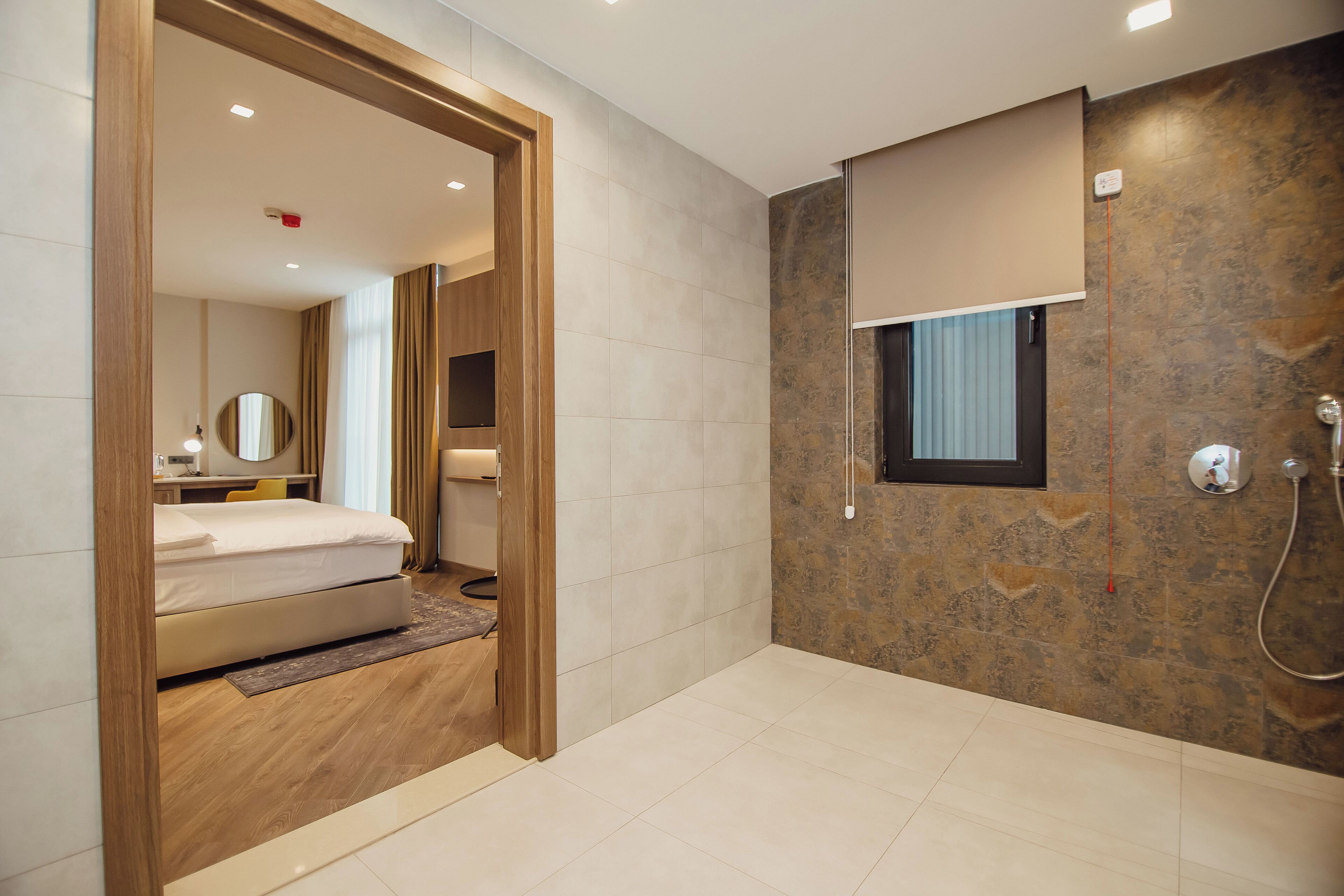 Habitación de hotel moderna con una puerta de madera que da a un baño, una cama, un escritorio con silla y un espejo grande.