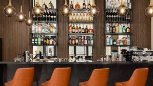 A bar area with multiple shelves of liquor bottles, a coffee machine, and three orange bar stools. - La Quinta by Wyndham Batumi (Batumi)