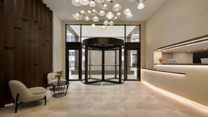 A modern lobby with a revolving door, a reception desk, and a seating area with a vase of flowers. - La Quinta by Wyndham Batumi (Batumi)