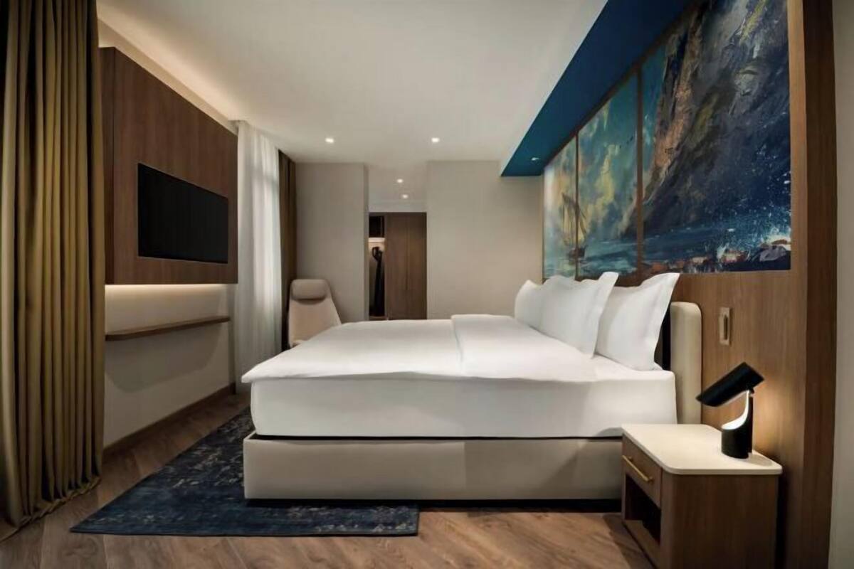 Camera da letto moderna con un letto grande, una TV a schermo piatto, un quadro e un comodino con una lampada.