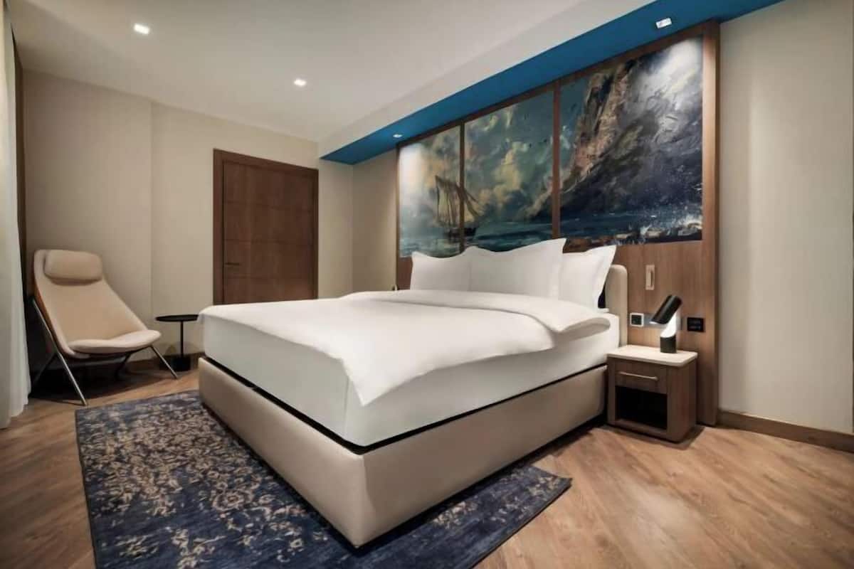 Una camera d'albergo moderna con un letto grande, una sedia, un comodino e un quadro appeso al muro.