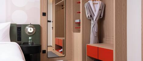 A hotel room with a bed, a mirror, a robe hanging, a red storage unit, and a small exercise mat.