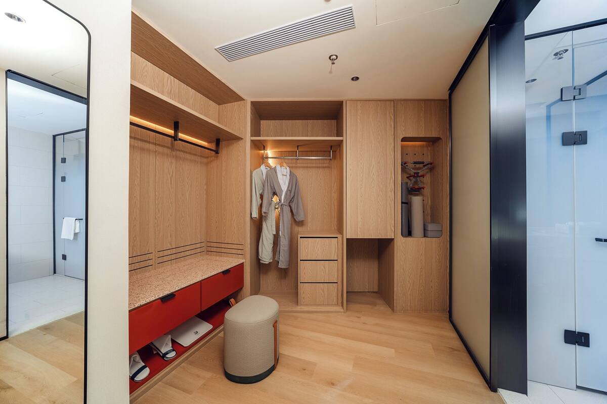 A modern bathroom with a shower, a vanity with a red countertop, and a wooden vanity with drawers.