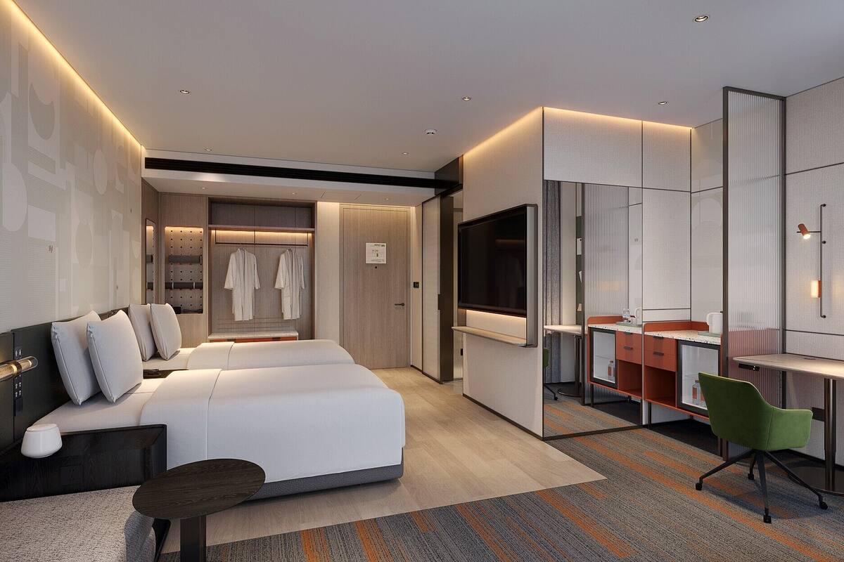 A modern hotel room with a large bed, a desk, a mirror, and a seating area.