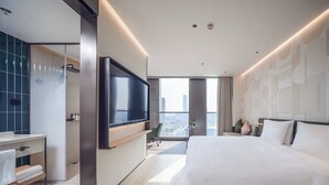 A modern hotel room with a large bed, a flat-screen TV mounted on the wall, a bathroom with a glass shower enclosure, and a city view through the window. - EVEN Hotel Shanghai Jinqiao by IHG (Shanghai)