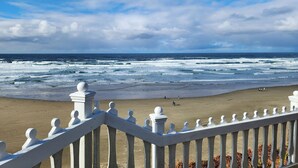 A beach with waves, a white fence, and a clear sky.