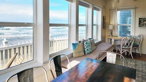 A room with a view of the ocean, a wooden table, a cushioned bench, and wicker chairs.