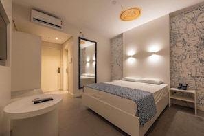 A bedroom with a bed, bedside table, mirror, wall art, and an air conditioning unit.