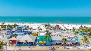 A beachside hotel with multiple buildings, a parking lot, and a pier extending into the ocean.