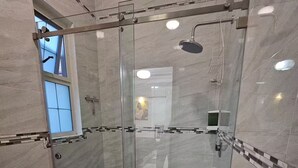 A modern bathroom with a glass-enclosed shower, a toilet, and a stack of towels. - Casa Real Hotel (Degollado)