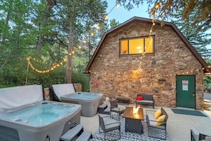 Une cabane en pierre avec un jacuzzi, un espace salon extérieur et des guirlandes lumineuses.