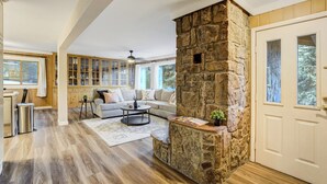 Un salon spacieux avec une cheminée en pierre, un canapé, une table basse et une vue sur l’extérieur.