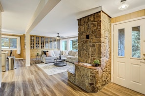 A spacious living room with a stone fireplace, a sofa, a coffee table, and a view of the outdoors.