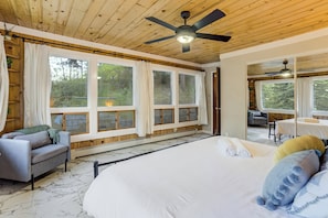 A bedroom with a large bed, a ceiling fan, and a view of the outdoors.