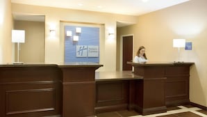 Área de recepção com a placa Holiday Inn Express, duas luminárias fixadas na parede e um balcão de check-in.