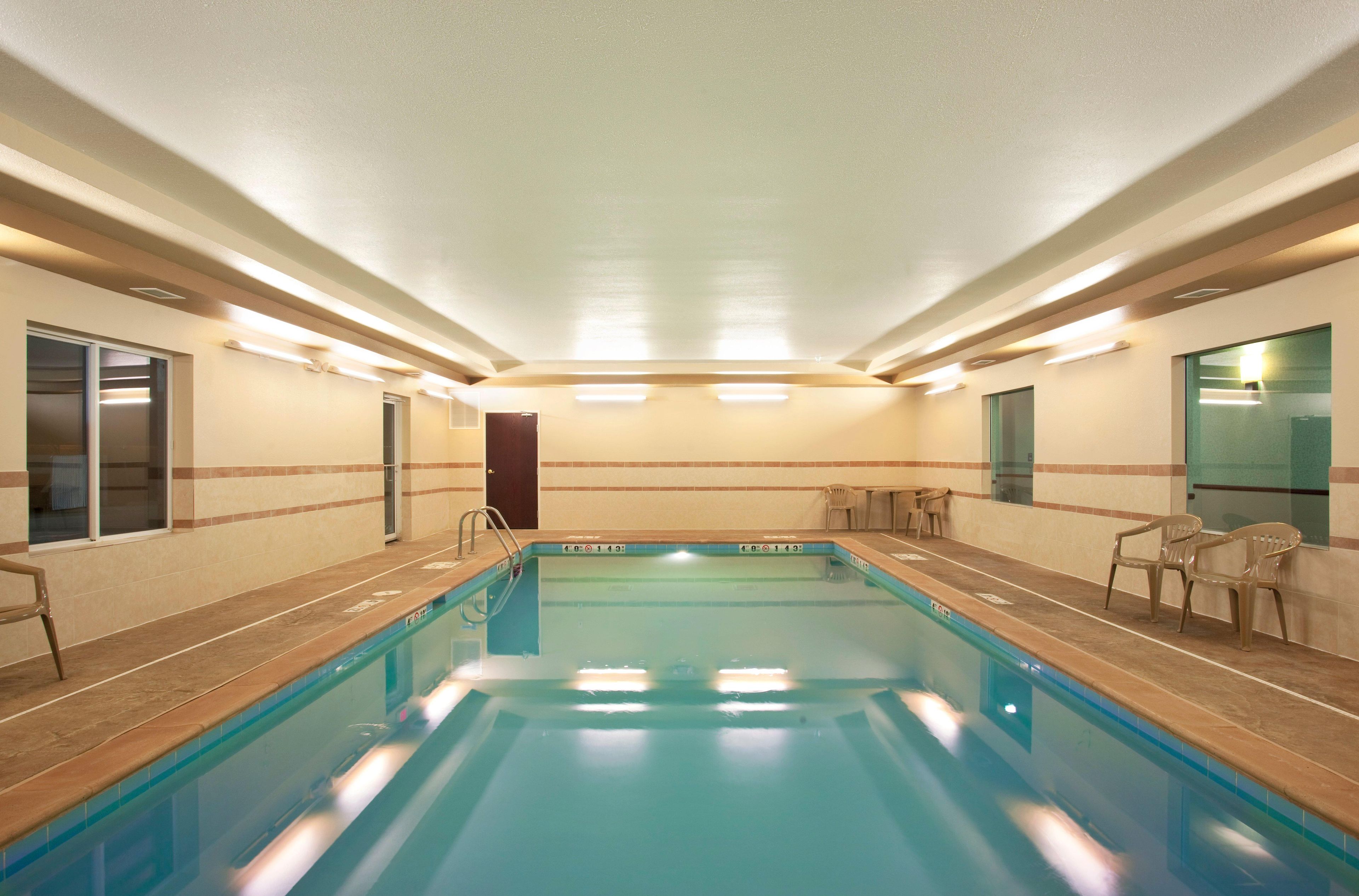 An indoor swimming pool with a tiled floor, a ladder, and chairs along the sides.