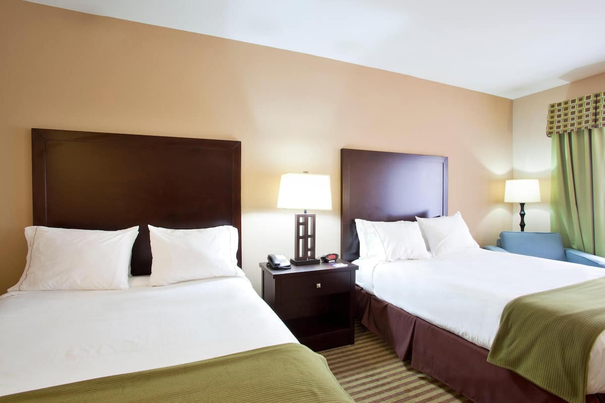 A hotel room with two beds, a nightstand with a lamp, and a window with curtains.