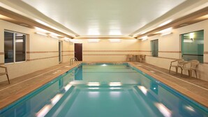 Piscina interna com chão em mosaico, escada e cadeiras nas laterais.