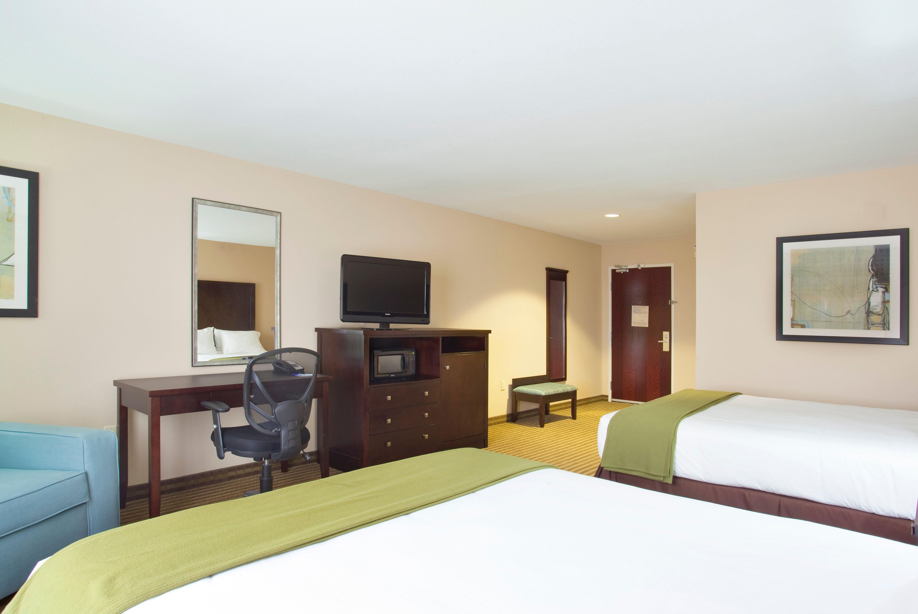 A hotel room with two beds, a desk with a chair, a television, a mirror, and a door.