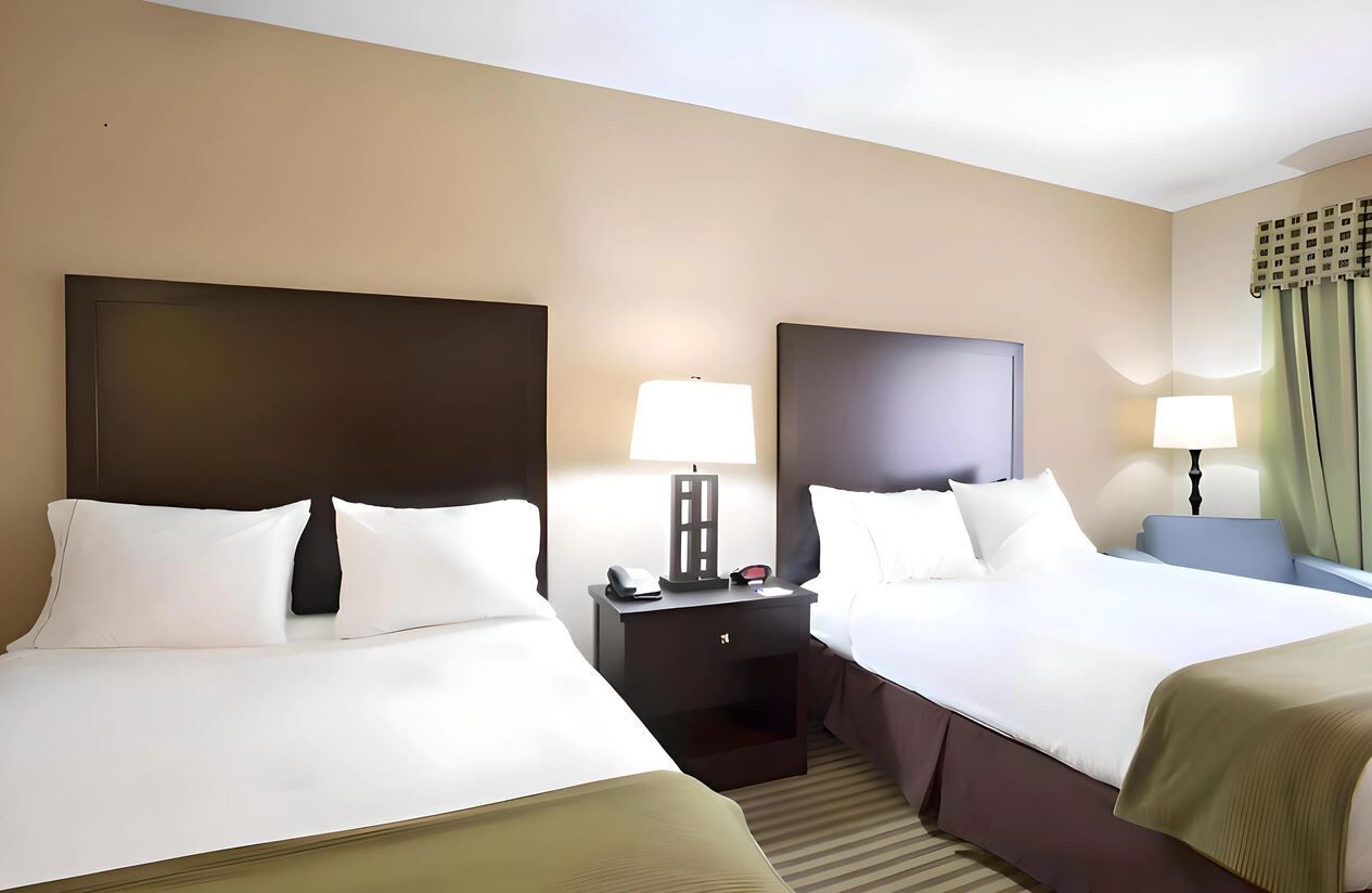 A hotel room with two beds, bedside tables, lamps, and a window with curtains.