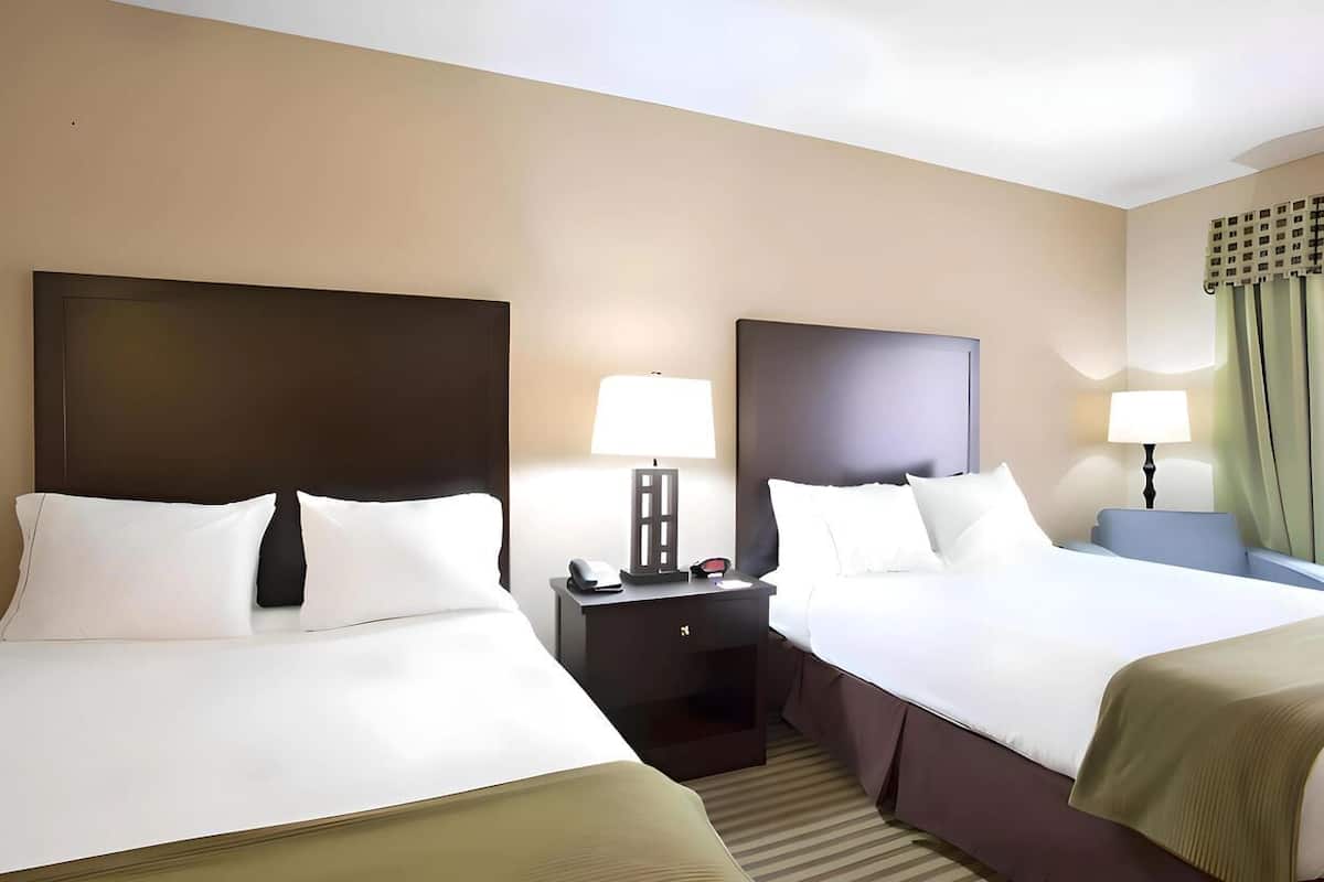 A hotel room with two beds, bedside tables, lamps, and a window with curtains.