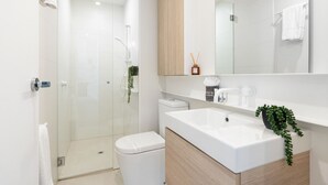 A modern bathroom with a glass-enclosed shower, a white toilet, and a sink with a wooden cabinet. - Urban Living at Its Best (Carnegie)