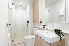 A modern bathroom with a glass-enclosed shower, a white toilet, and a sink with a wooden cabinet. - Urban Living at Its Best (Carnegie)