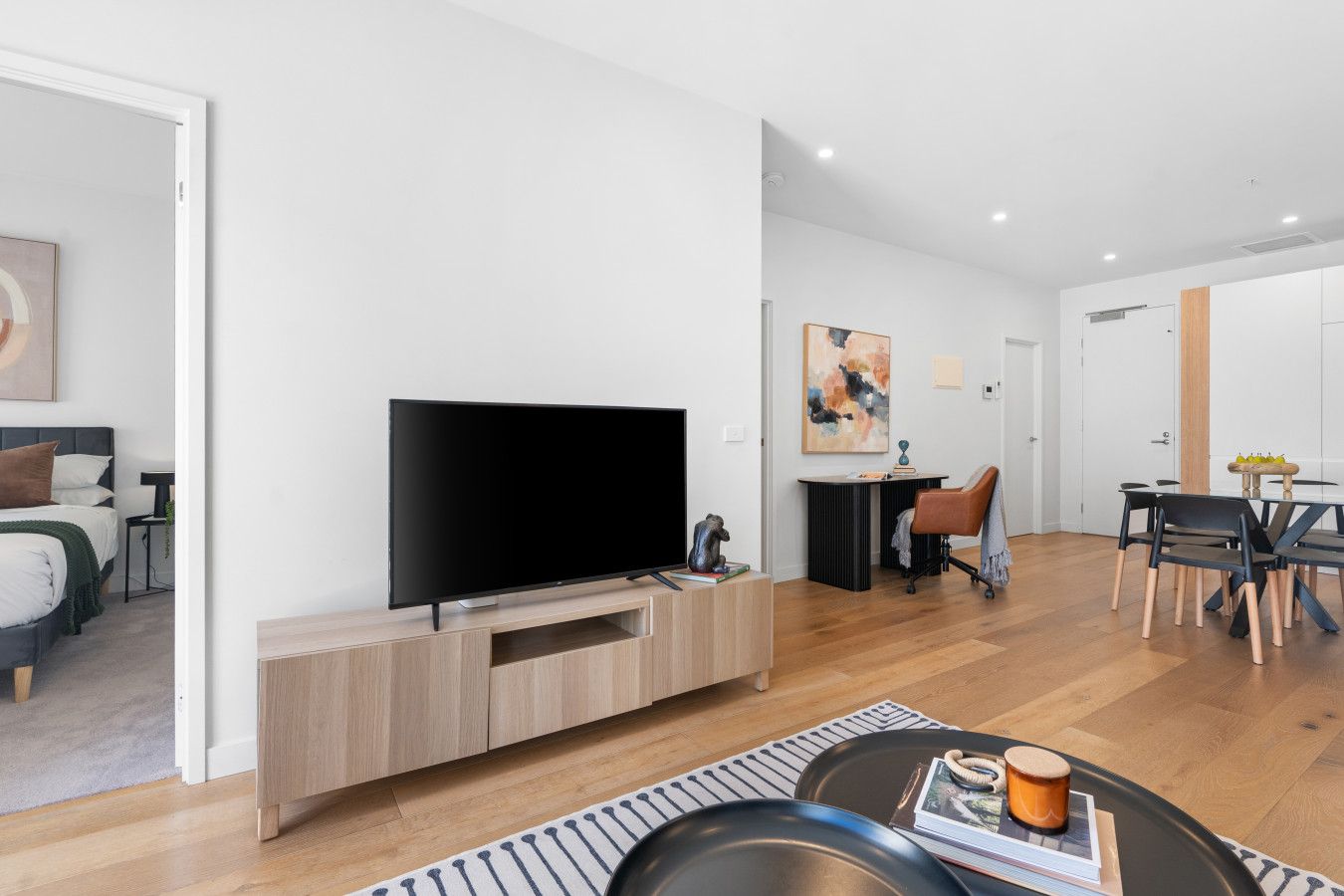 Un salon moderne doté d’un téléviseur à écran plat, d’un meuble de rangement en bois et d’un coin repas avec une table et des chaises.