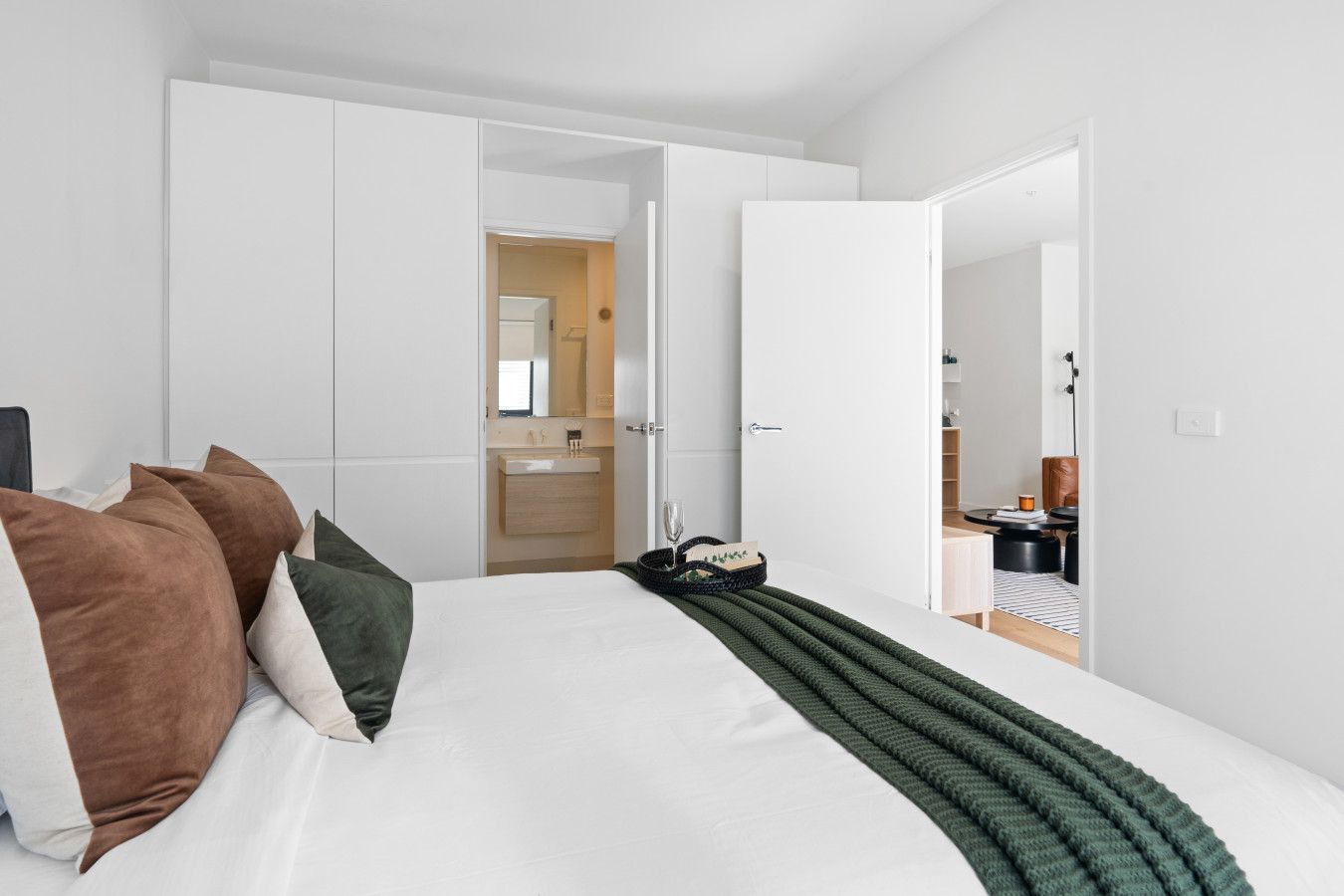 A modern bedroom with a large bed, white walls, and a visible bathroom in the background.