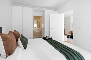 Ein modernes Schlafzimmer mit einem großen Bett, weißen Wänden und einem sichtbaren Badezimmer im Hintergrund.