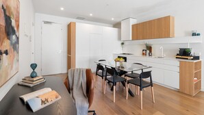 A modern kitchen with white cabinets, a wooden countertop, and a dining area with a glass table and black chairs. - Urban Living at Its Best (Carnegie)
