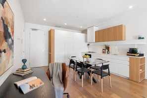 A modern kitchen with white cabinets, a wooden countertop, and a dining area with a glass table and black chairs. - Urban Living at Its Best (Carnegie)