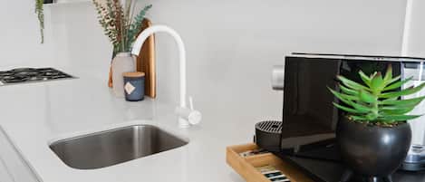 Una cocina moderna con un lavamanos de acero inoxidable, un grifo blanco, una estufa negra y una bandeja de madera con varios objetos.