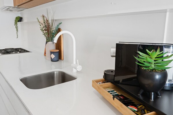 A modern kitchen with a stainless steel sink, a white faucet, a black stove, and a wooden tray with various items.