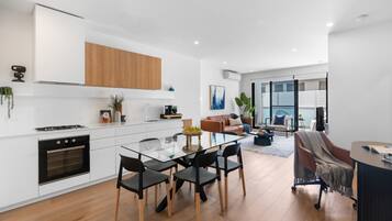 A modern kitchen with white cabinets, a built-in oven, and a dining area with a glass table and chairs.
